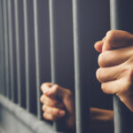 Man in prison hands of behind hold Steel cage jail bars. offende