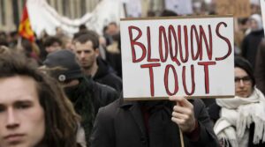 Manifestation : une personne tient une pancarte « BLOQUONS TOUT » au milieu d’une foule