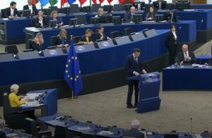 Jordan Bardella prend la parole à la tribune du Parlement européen à Strasbourg, devant le drapeau de l’UE, tandis que des élus et membres de la Commission siègent en arrière-plan.