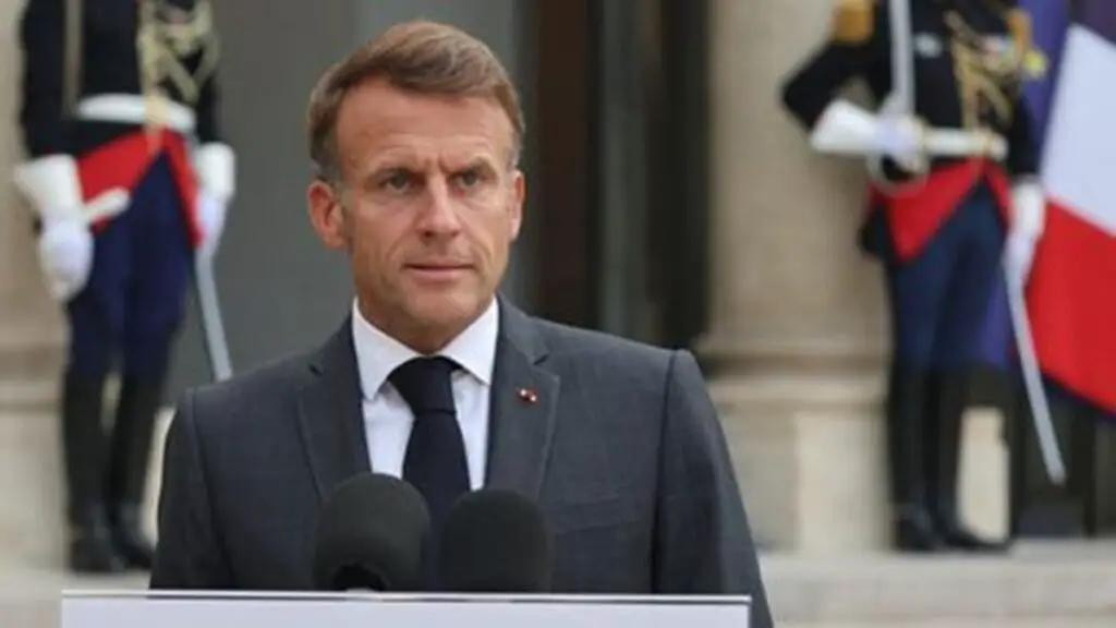 Emmanuel Macron s’exprime derrière des micros, avec des gardes en uniforme et un drapeau tricolore en arrière-plan