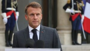 Emmanuel Macron s’exprime derrière des micros, avec des gardes en uniforme et un drapeau tricolore en arrière-plan