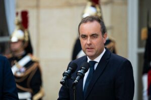 Sébastien Lecornu s’exprime devant deux micros, en extérieur, avec des gardes républicains flous en arrière-plan dans la cour d’un bâtiment officiel.