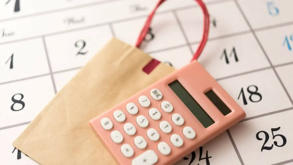 Calculatrice rose posée sur un calendrier, glissée dans un petit sac en papier, symbole des nouveaux tarifs et règles entrant en vigueur au 1er septembre.