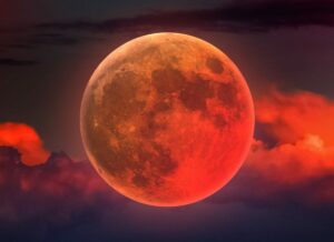 Gros plan d’une éclipse totale de Lune : disque rouge cuivré, dit « Lune de sang », au-dessus de nuages sombres.