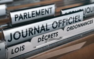 Gros plan sur un classeur intitulé « Journal officiel » avec des intercalaires « Décrets », « Lois » et « Ordonnances », illustrant les publications légales en France.
