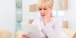 Femme retraitée, l’air inquiet, lit un relevé de pension chez elle.